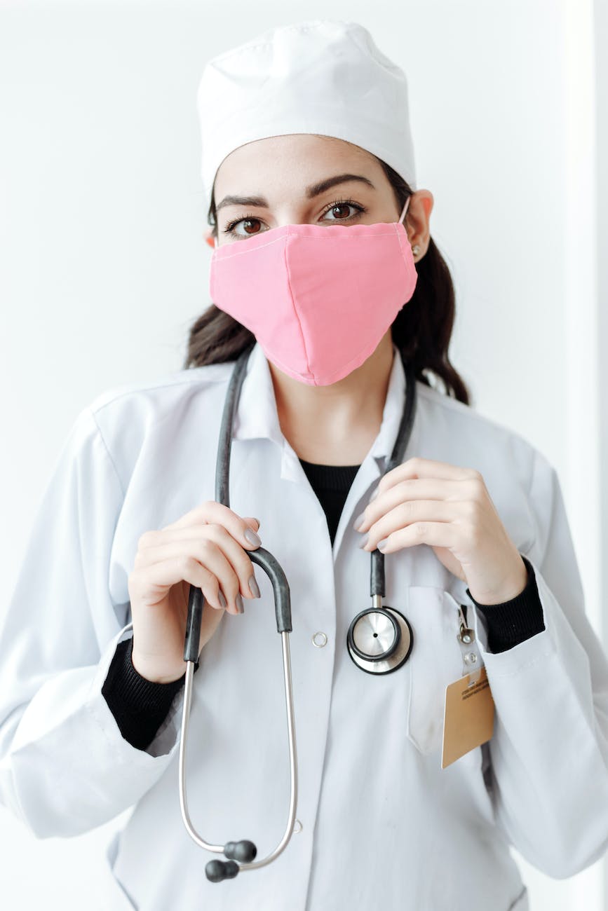 a doctor with stethoscope wearing pink face mask while looking at the camera